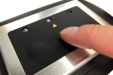 Close-up of a finger pressing a capacitive touch button on a black and silver control panel.